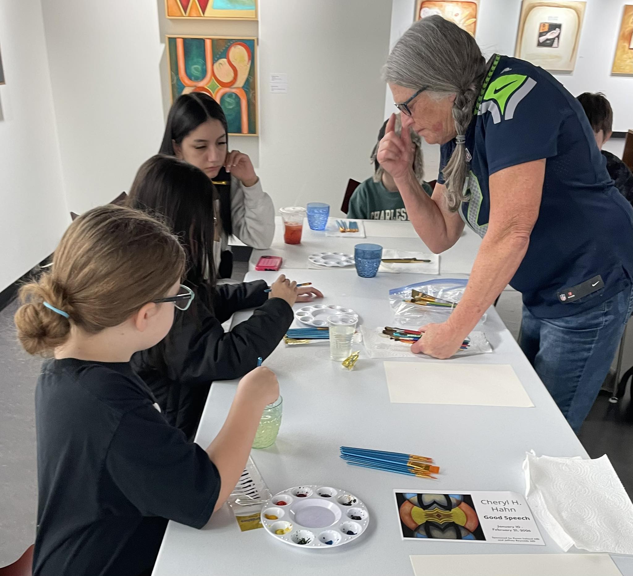 an instructor giving students feedback who are doing water color in class at an art gallary